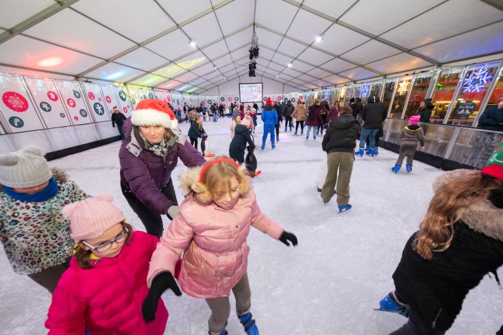 A mix of children and adults whizz around an indoor ice rink.