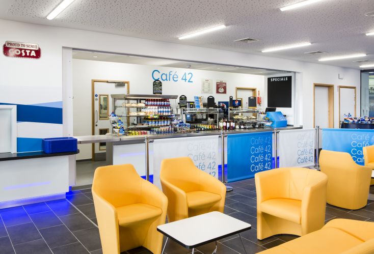 A bright cafe with yellow chairs and a bar with drinks and snacks. Behind the bar is signage saying Cafe42.