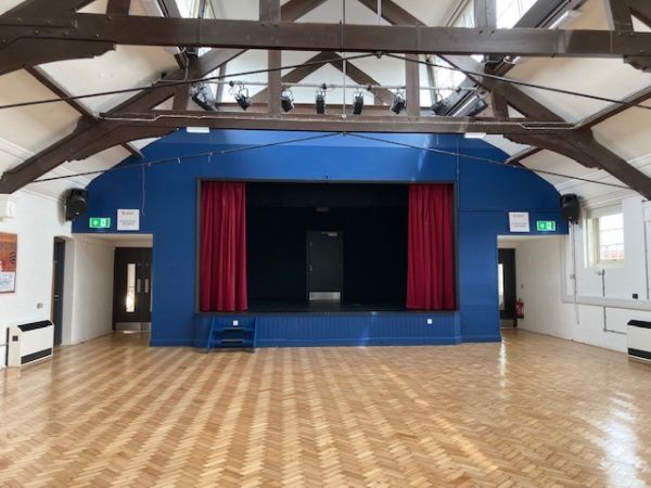 long view of stage with blue curtains and wooden floor in large hall
