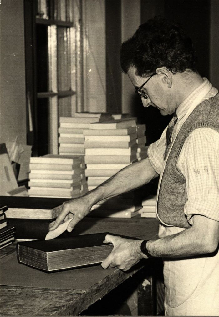 man with white apron standing at desk, looking at the books