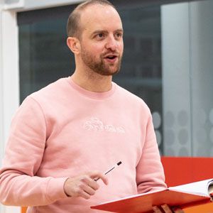 Actor Roddy Peters. He is a young man with short brown hair. He is wearing a light pink jumper and holding a book.