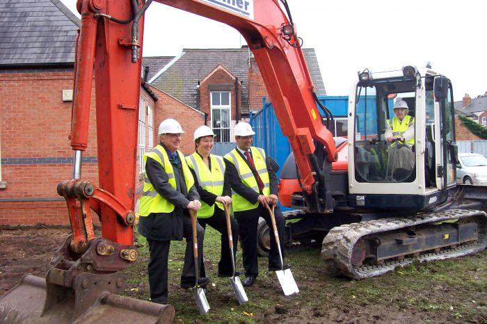 excavator with women driving and 3 people stood on the ground with shovels