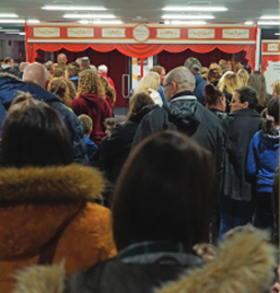 A picture of lots of people standing in a well-lit room waiting in front of doors