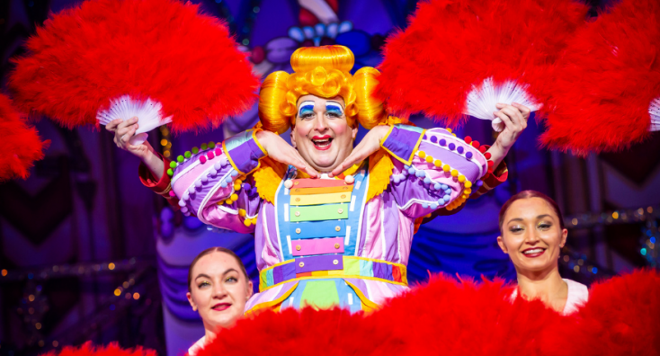 A male actor playing a female character dressed in a bright, colourful dress with an orange wig.