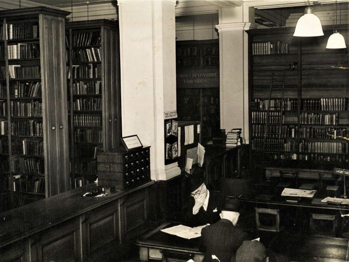 wide view of the library book shelfs and a table with a man reading a book