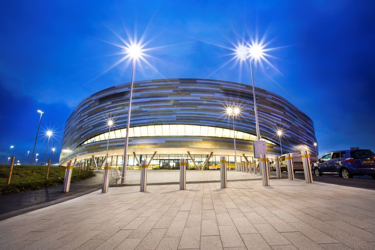 A picture of Derby Arena, a round, gold coloured building photographed at night with the lights on.