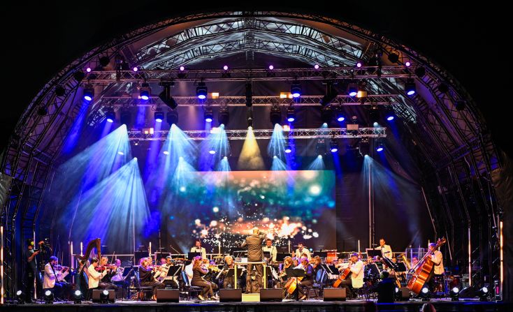 An orchestra plays on an outdoor stage.