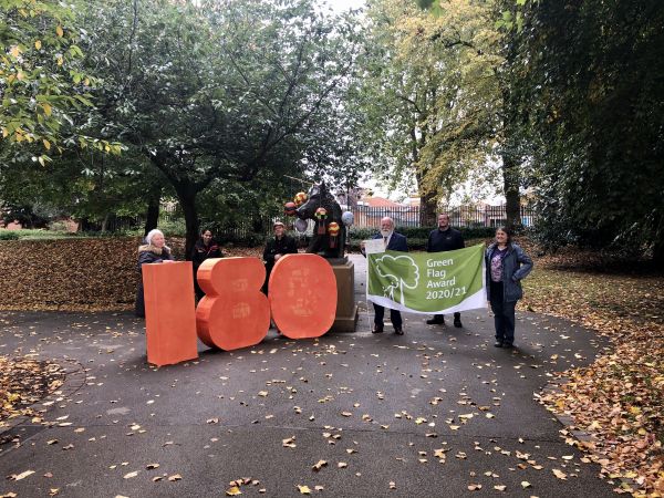 Councillor Robin Wood holds the Green Heritage award plaque at Derby Aboretum, with park rangers and members of the Friends of Derby Arboretum. The giant 180 was made by Spiral Arts for the 180th anniversary, while the model hot air balloons were made for